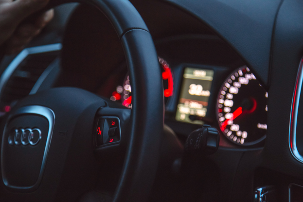 Eine Person fährt nachts ein Auto, mit einer Hand am Lenkrad, während das Armaturenbrett, einschließlich des Tachometers, zu sehen ist.