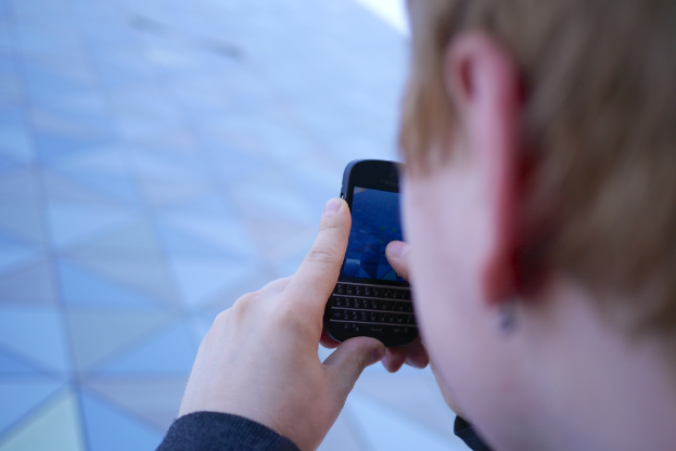 Eine Person mit einem Mobiltelefon auf der Straße stehend.