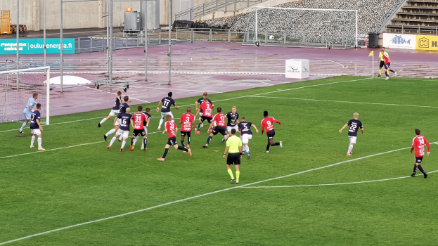 Eine Gruppe von Menschen, die Fußball auf einem Feld spielen, mit Zuschauern im Hintergrund eines Stadions.