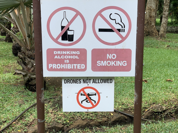 Verbotsschild für Alkoholkonsum und Rauchen mit Bäumen und Gras im Hintergrund.
