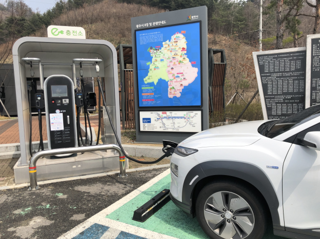 Elektrisches Auto an einer Ladestation in Seoul, Südkorea, mit Bäumen und Himmel im Hintergrund.