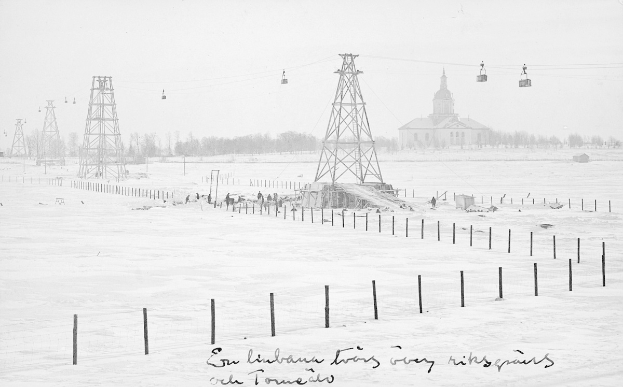 Schwarze-Weiß-Foto eines Skilifts in einer verschneiten Wiese mit Stützpfählen, Überseilbahn, Bäumen und einem Gebäude im Hintergrund, mit Text am unteren Rand.