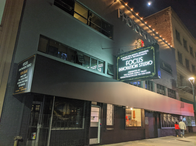 Außenansicht des Focus Innovation Studios in New York City bei Nacht, mit beleuchteten Gebäuden, Fußgängern auf dem Gehweg und sichtbarem Himmel.