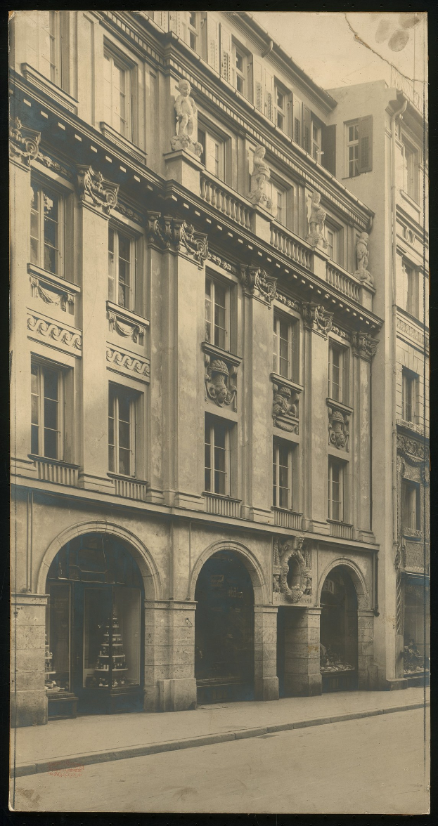 Altes Gebäude mit zahlreichen Fenstern und dekorativen Skulpturen an seiner Fassade, das sich entlang einer belebten Stadtstraße befindet.