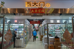 Innenansicht einer chinesischen Apotheke mit Glaswänden, Regalen voller Artikel, verstreuten Kartons, einer Pflanze links und einem Schild oben, das darauf hinweist, dass es sich um eine chinesische Drogerie handelt.