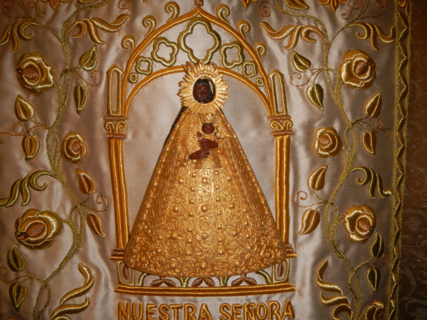 Goldbestickte Chasuble mit einer serenen Frau in einem hochgeschlossenen, langärmeligen Kleid mit einem Dutt, umgeben von kunstvollen Texten und goldenen Verzierungen.
