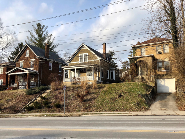 Reihe von Häusern entlang einer Straße mit Fenstern, Türen, Säulen, Geländern, Stufen, Pflanzen, Gras, Bäumen und einem Wegweiser, unter einem bewölkten Himmel, repräsentiert eines der teuersten Häuser zum Verkauf in Detroit.