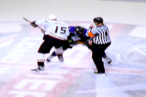 Drei Personen mit Helmen, Kleidung und Ski-Stiefeln nebeneinanderstehend.