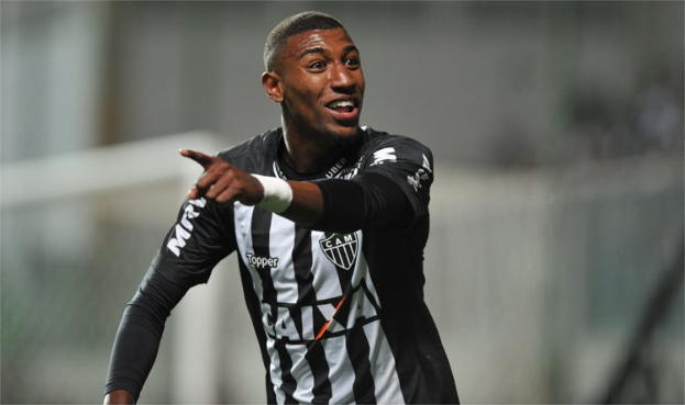 Fußballspieler in schwarzer und weißer gestreifter Jerseys, der grinsend ein Tor feiert, Hintergrund unscharf.