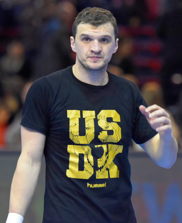 Ein Mann in schwarzem T-Shirt und weißen Shorts steht auf einem Platz, mit der Aufschrift "Hummel USA vs Germany" unten.