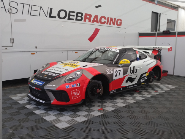 Ein Porsche 911 GT3 RSR Rennauto in einer Garage mit einer Wandmontage und einer Tür im Hintergrund.