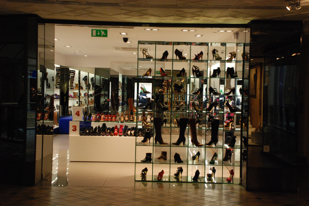 Eine Schuhgeschäftsauslage mit verschiedenen Schuhen und Sandalen auf einem weißen Tisch, mit einer Wand und Decke im Hintergrund.