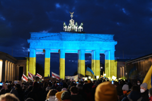 Eine Menschenmenge steht vor dem Brandenburger Tor in Berlin, Deutschland, mit Fahnen und Plakaten, auf denen eine Fahne auf der rechten Seite zu sehen ist.