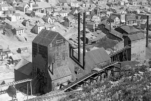 Schwarz-weiß-Foto einer industriellen Stadt mit Gebäuden, Häusern, Strommasten, Bäumen, Schienen, wahrscheinlich mit einem Kohlebergwerk im Vordergrund.