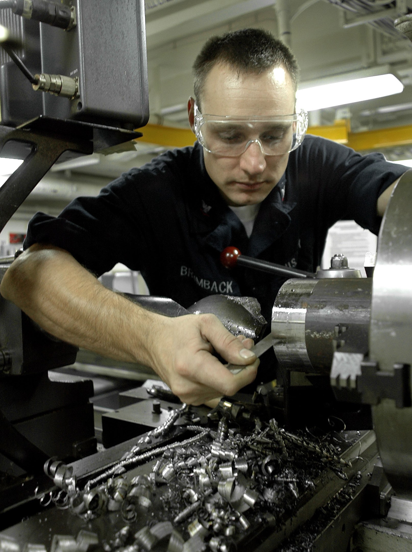 Ein Monteur mit Schutzbrille bedient eine Maschine in einer gut beleuchteten Fabrikumgebung.