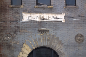 Ein Backsteinbau mit einer Tafel, auf der 'Stadt' steht, mit einer Tür unten und Fenstern mit einer Namensschilder oben.