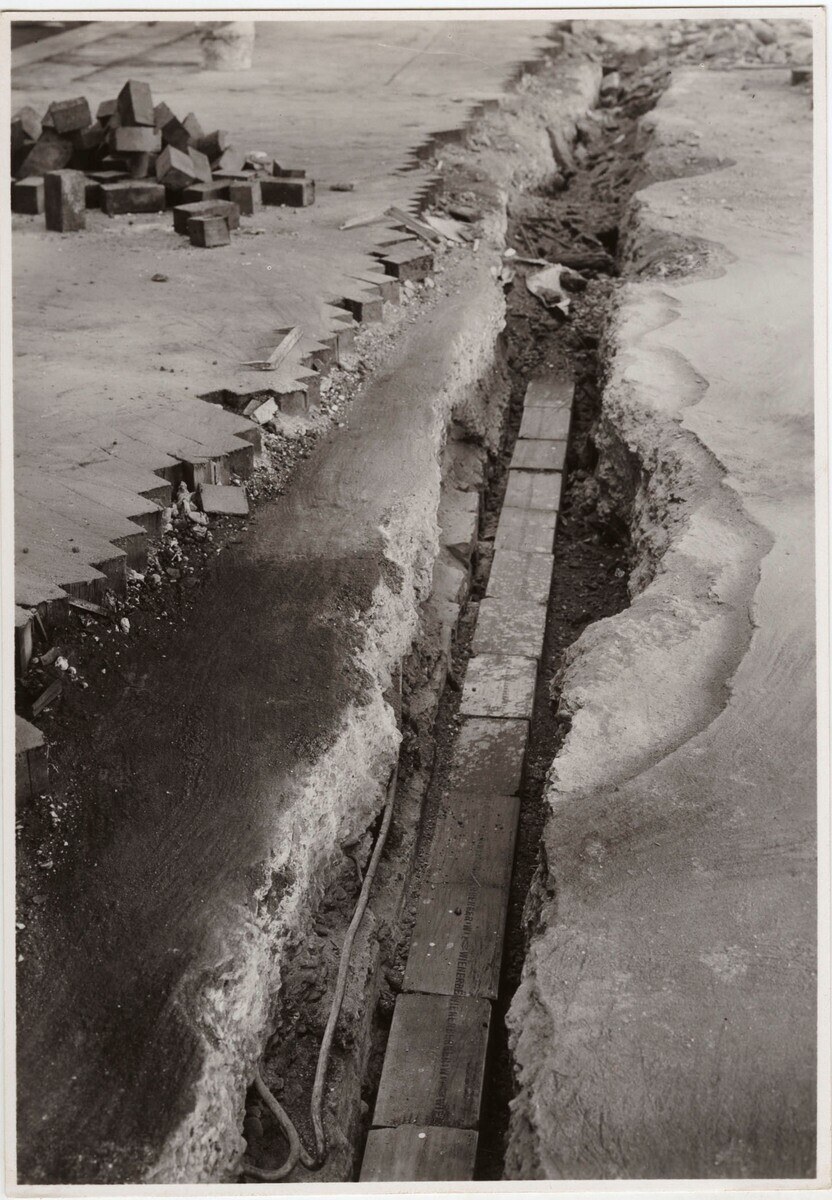 Schwarzes und weißes Foto einer Straße mit einem großen Riss darin und verstreuten Ziegeln auf der linken Seite.