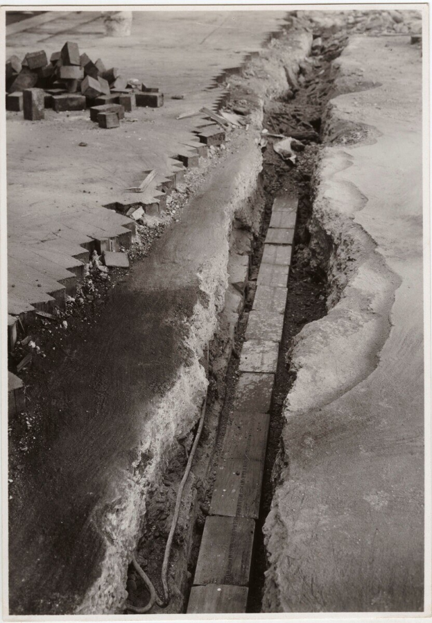 Schwarzes und weißes Foto einer Straße mit einem großen Riss darin und verstreuten Ziegeln auf der linken Seite.
