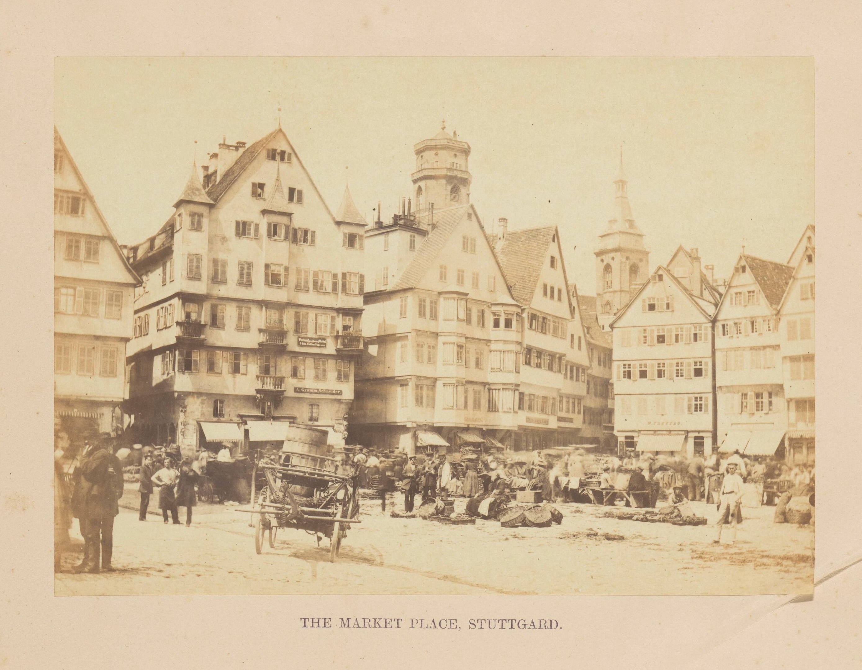 Altes Schwarz-Weiß-Foto eines belebten Marktplatzes in Stuttgart, Deutschland, mit mehrstöckigen Gebäuden, Fußgängern, Pferdewagen und verschiedenen Marktständen, mit handgeschriebener Text am unteren Rand.