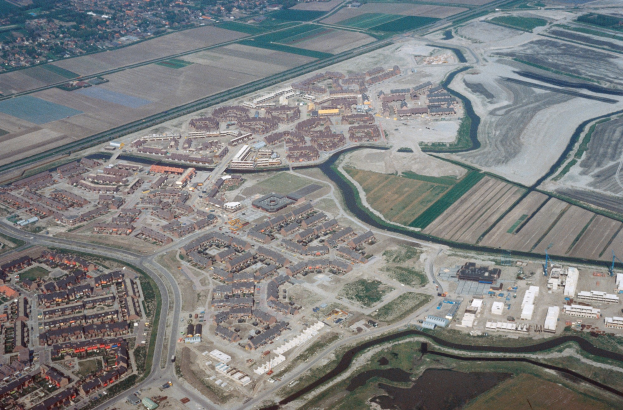 Luftaufnahme einer Stadt mit Gebäuden, Straßen, Feldern, Bäumen und einem zentralen Reservoir, das von städtischen Gebieten umgeben ist.