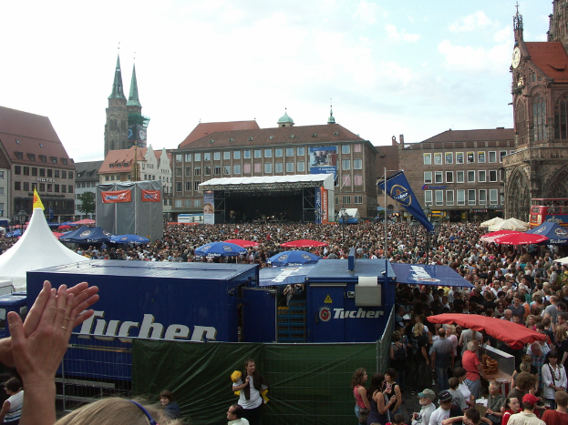 Eine Gruppe von Menschen versammelte sich vor Gebäuden mit Fenstern, hielt Schirme und ein Banner hoch.