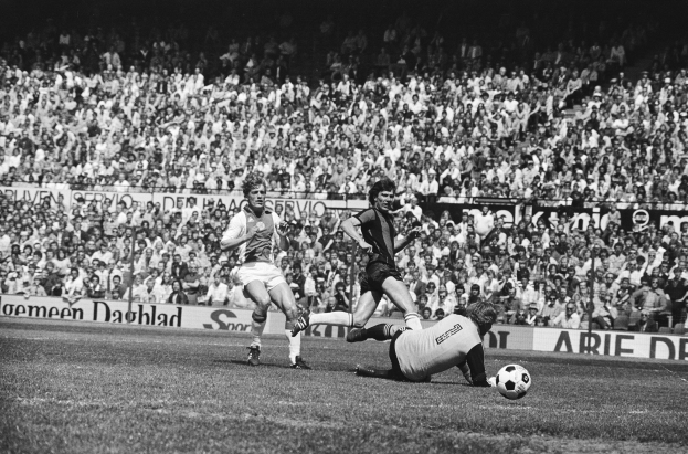 Schwarzes Foto von Männern, die Füßball auf einem Feld spielen, mit Zuschauern im Hintergrund und einer Tafel mit der Aufschrift "Bundesliga 1978-79 Ajax 1-1 Hannover 96".