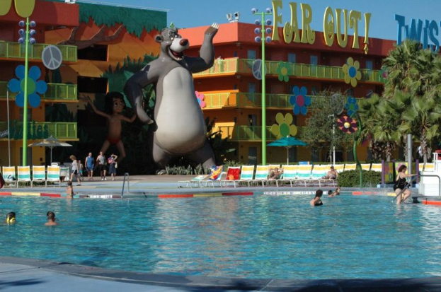 Ein Schwimmbad mit blauem Wasser und Menschen darin, mit Cartoon-Bildern und Polen im Hintergrund.