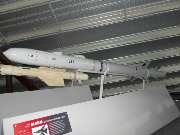 Raketen werden mit weißen Tafeln am Boden, einer davon mit einem roten und grauen Plakat mit gedrucktem Text, und einem weißen Dach oben gezeigt.