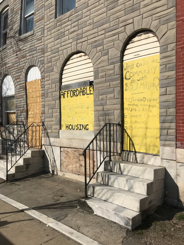 Verschlossenes Gebäude mit 'Bezahlbarer Wohnraum'-Schild, Treppe mit Geländer und Straße unten.