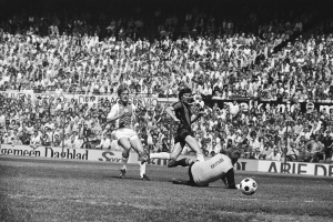 Schwarzes Foto von Männern, die auf einem Feld Fußball spielen, mit Zuschauern im Hintergrund und einer Tafel "Bundesliga 1978-79 Ajax 1-1 Hannover 96".