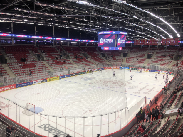 Hockey-Spiel in einer großen Arena mit Zuschauern, eine Eisfläche umgeben von einem Zaun, ein Display, das "St. Louis Blues vs Detroit Red Wings" anzeigt, Metallrahmen, ein Dach mit Deckenleuchten und ein Dach.