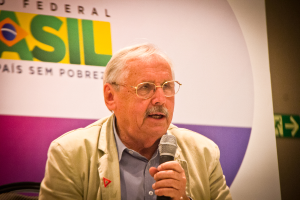 Eine Person, die in ein Mikrofon spricht und von einem Banner mit der Aufschrift 'Bundes' umgeben ist.