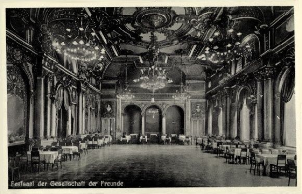 Schwarz-weiß-Foto eines großen Raums mit Tischen, Stühlen, Säulen, Bögen und Deckenleuchter, beschriftet mit "Festival der Gesellschaft der Freunde, Berlin" unten.