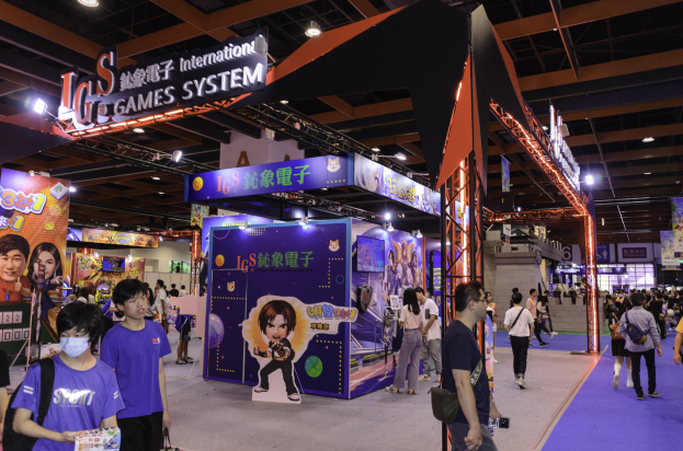 Eine Gruppe von Menschen, die durch einen Convention-Saal auf einer Gaming-Messe in China gehen, einige tragen Taschen und halten Gegenstände, mit Display-Boards, Deckenbeleuchtung und Teppichboden.