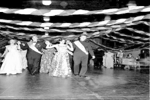 Eine Gruppe von Menschen, die auf einem beleuchteten Tanzboden mit Bändern tanzen, dargestellt in Schwarz-Weiß.