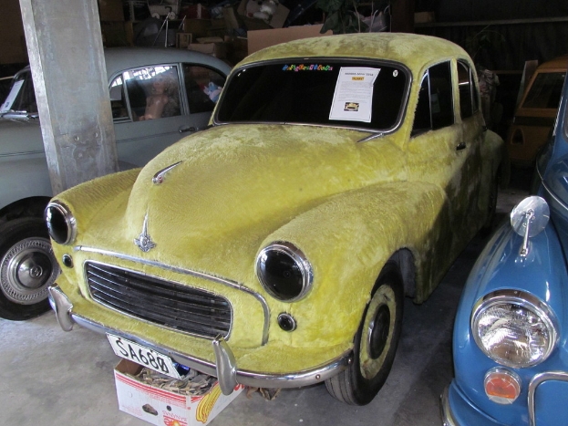 Verschiedene Oldtimer sind vor einer Wand mit diversen Accessoires geparkt, wobei auf der linken Seite eine Säule zu sehen ist.
