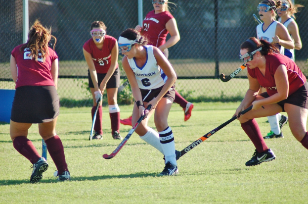 Frauen beim Hockey auf einem Rasenfeld mit einem Netz als Hintergrund.