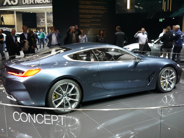 Ein BMW 8er-Konzeptfahrzeug mit glänzendem Schwarz und Chromakzenten wird auf der IAA in Frankfurt präsentiert, umgeben von Menschen, die Fotos machen, mit einem hell beleuchteten Hintergrund und einem Textschild.