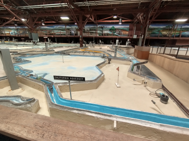 Ein großer Indoor-Wasserpark mit zahlreichen Wasserrutschen, Pfählen, Texttafeln, Deckenleuchten und Wandgemälden, der wie ein Minigolfplatz gestaltet ist.