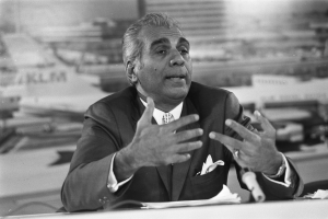 Ein Mann in einem Anzug sitzt an einem Tisch mit Papieren und einem Mikrofon, unscharfer Hintergrund legt den Fokus auf ihn als Bürgerrechtsführer.