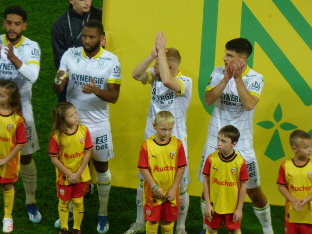 Eine Gruppe von Fußballspielern in Uniform klatscht auf einem Ligue-1-Feld in celebration, mit einem "Ligue-1"-Schild im Hintergrund.