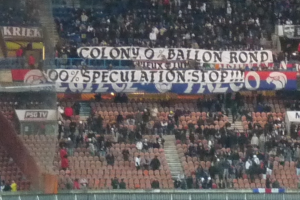 Ein Stadion mit einer großen Menschenmenge, Bannern und Stühlen, mit einem Zaun unten und einer Treppe links.