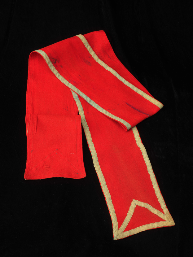 Ein roter Umhang mit goldener Borte auf schwarzem Hintergrund.