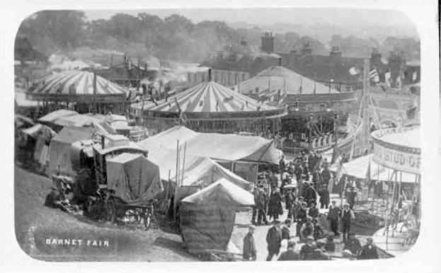 An old black and white photo of a bustling carnival scene with tents, people, carts, and buildings in the background, labeled "Barnet Fair, London, England".