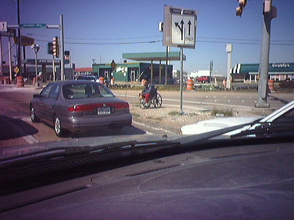 Ein Autospiegel, der mehrere Fahrzeuge, Häuser, Pfosten mit Signalbeleuchtung und Überlandleitungen reflektiert.
