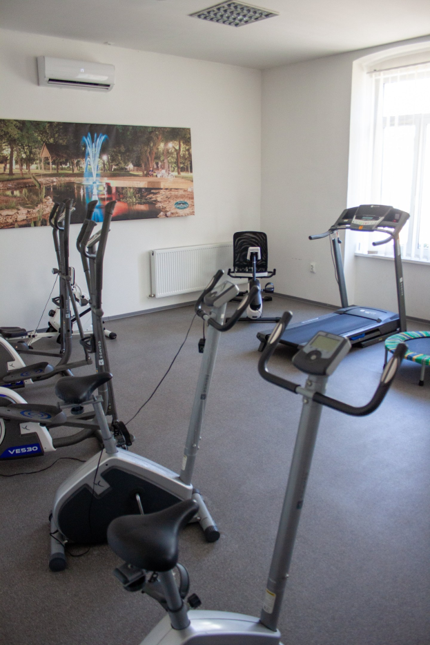 Ein Fitnessstudio-Innenraum mit Geräten wie Laufbändern und Ellipsotrainern, einem gerahmten Foto an der Wand, einer Klimaanlage und einem Fenster auf der rechten Seite.