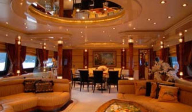 Eine Hotellobby mit Sofas, Stühlen, Tischen und Blumenarrangements im Vordergrund, Fenstern mit Vorhängen und Lampen auf beiden Seiten, einem gerahmten Bild und einer Lampe im Hintergrund sowie einem Spiegel mit Deckenleuchten oben.