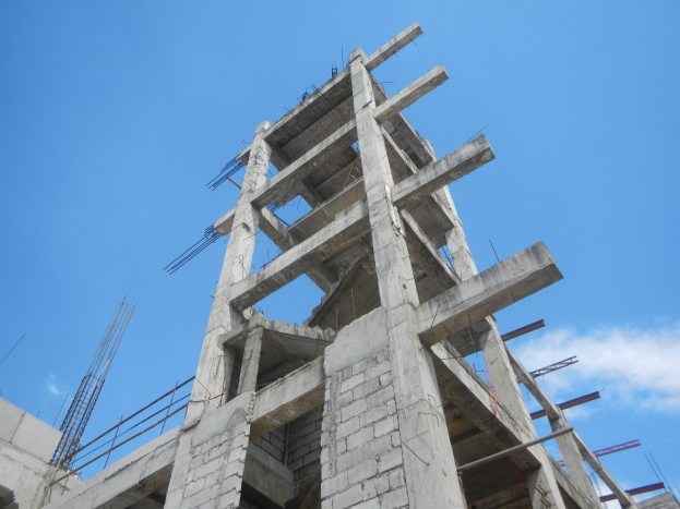 Ein hohes Betongebäude im Bau mit Gerücsten und Eisenstangen, vor einem Himmel mit weißen Wolken.