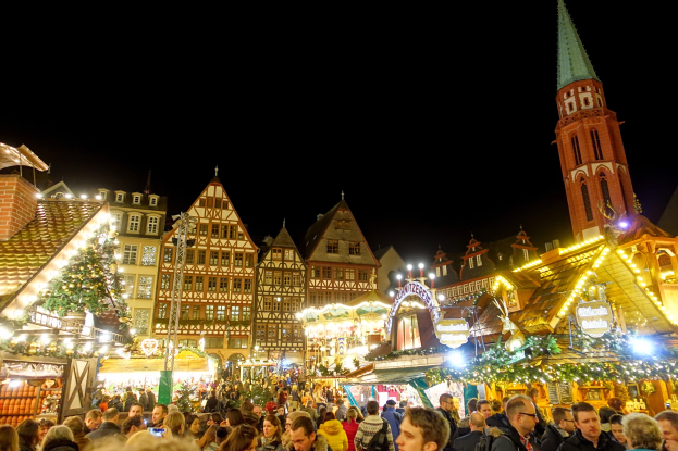 Ein lebendiger Weihnachtsmarkt in Nürnberg, Deutschland, mit Menschen um beleuchtete Stände, Gebäuden mit Fenstern und einem Kirchturm unter einem dunklen Himmel.