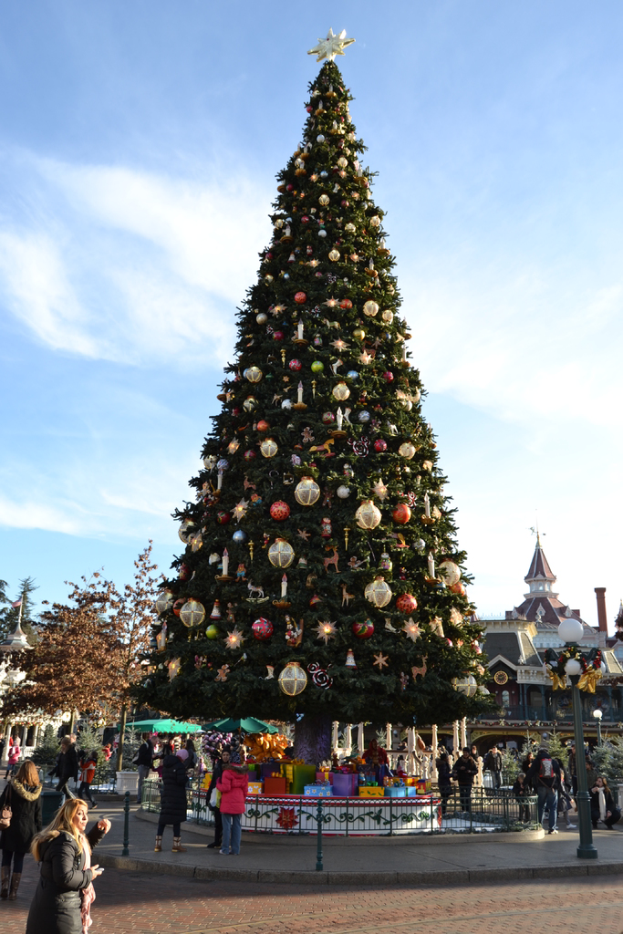 Ein dekorativer Weihnachtsbaum mit einem schwarzen Zaun davor, vor zwei Mädchen, die sich unterhalten, mit einem Schloss im Hintergrund.